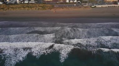 Bir rıhtımın yakınındaki kumlu bir sahilde yuvarlanan güzel bir denizin hava manzarası.