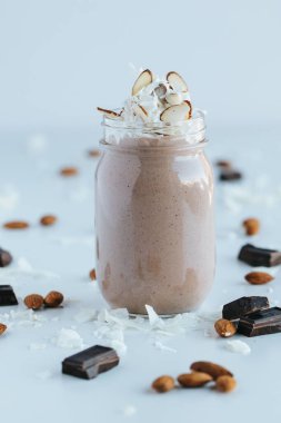 Çikolatalı protein karışımının bir kavanozda dikey görüntüsü. Masada çikolata dilimleri ve bademler var.