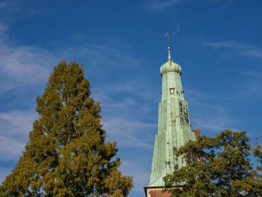 Almanya 'daki Raesfeld kalesinin kulesi ve mavi gökyüzüne karşı yeşil yapraklı ağaçlar.