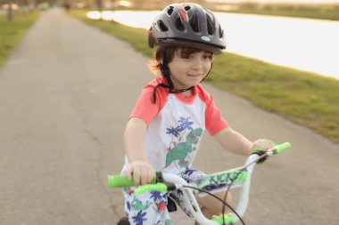 Nehir kıyısında kaskla bisiklet süren sevimli bir çocuğun yakın çekimi.