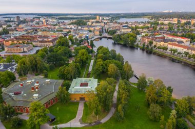Nehir ve bulutlu arka planda eski binalar olan bir kasabanın hava görüntüsü.