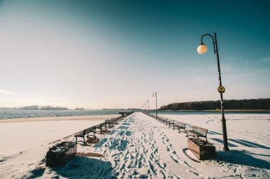Güneşli havalarda ahşap banklar ve lambalarla kışın manzarası.
