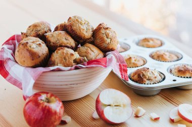 Muffinlere yakın plan beyaz bir kâse ve ahşap bir masa üzerinde elmalarla.