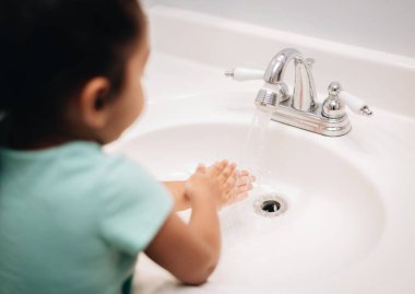 Temizlik pratiği yapan tatlı bir anaokulu kızı banyo lavabosunu yıkarken kullanıyor.