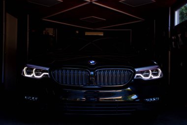 Siyah bir BMW 5G serisinin ön yüzü, logo ve LED ışıkları görünür.