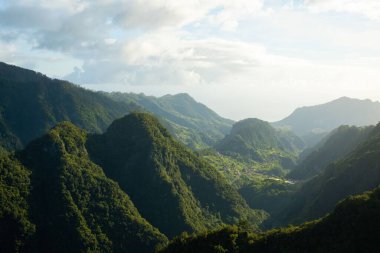 Ormanlarla kaplı yüksek dağların arka planda bulutlu mavi bir gökyüzü.
