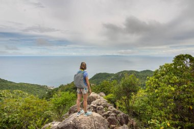 Kadın yürüyüşçü sırt çantasıyla uçurumda duruyor ve Tayland, Koh Tao 'da deniz manzarasını izliyor.