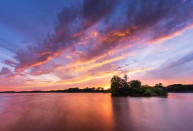 Durgun bir denizin uzun bir görüntüsü dramatik günbatımının parlak renklerini yansıtıyor.