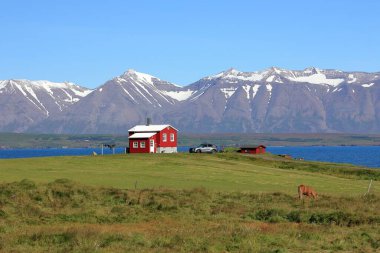 Küçük bir ev manzarası ve arka planda dağlar olan bir tepede park edilmiş bir araba.