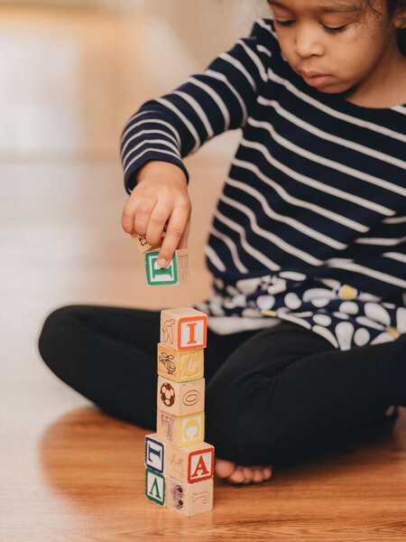 A preschool girl, playing with wooden letter blocks at home on the hardwood floor, the concept of early education