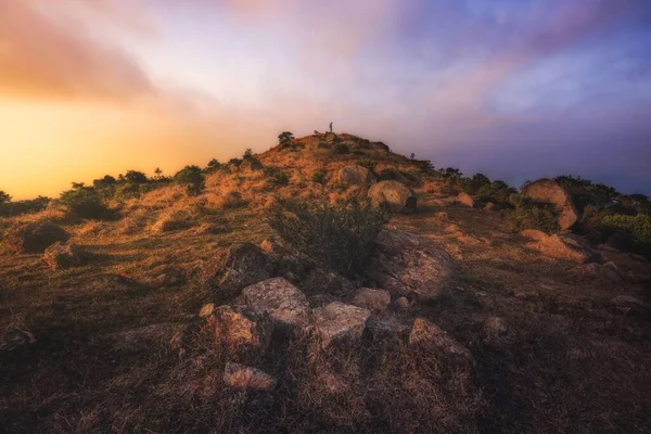 stock image A hill with dry grass over a background of colorful clouds during a sunset