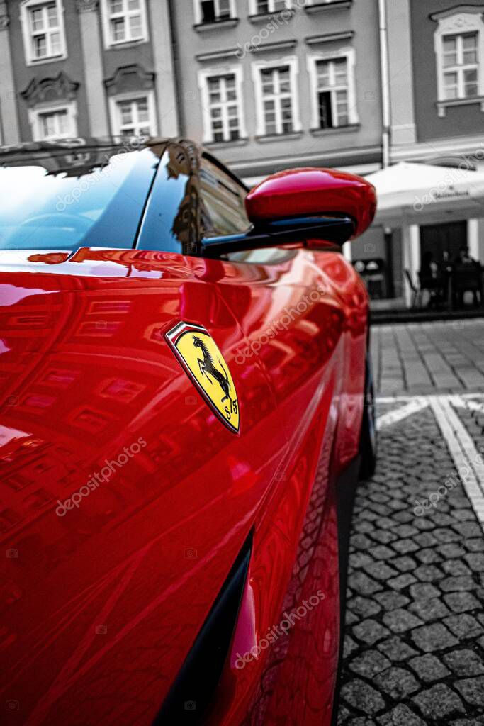 A vertical side view of a bright red Ferrari car parked on a street and its logo