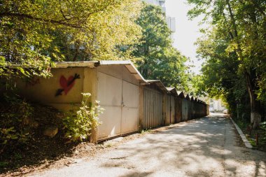 Güneşli bir sabahta yeşil yaprakların altında bir sıra eski garaj.