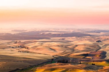 Toplanan buğday tarlasının üzerinde yuvarlanan tepe yüzeyi olan güzel renkli bir günbatımı manzarası.