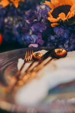 Tabak ve çatal bıçakların dikey yakın çekimi masanın üzerindeki çiçeklerle çevrili. Kutlama hazırlıkları.