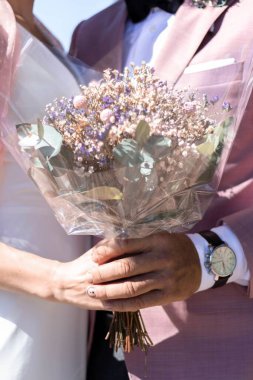 Düğün buketlerini gün ışığında tutan evli bir çiftin dikey görüntüsü.