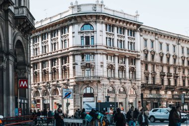 Milano, İtalya 'da kalabalık bir caddenin yatay görüntüsü, metro istasyonu ve arabaların yakınındaki insanlarla dolu.
