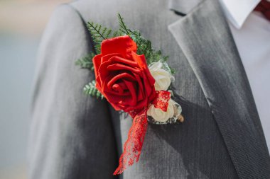 Düğününde gri takım elbiseli ve kırmızı güllü bir damadın yakın çekimi.
