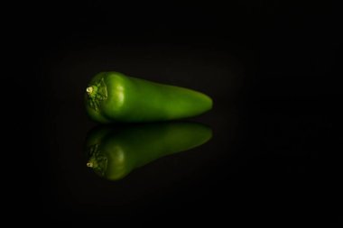 Siyah arkaplanda yansımalarla izole edilmiş yeşil biberin yakın çekimi.