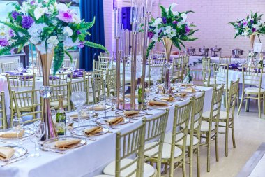 Masalar çatal bıçak ile döşenmiş ve bir düğün salonunda çiçek buketleriyle süslenmiş.