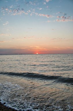 Batan güneşin ve dalgalı denizin üzerindeki renkli gökyüzünün dikey görüntüsü.