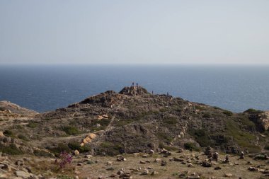 Bir grup yürüyüşçü tepenin üstünde dikiliyordu. Arka planda deniz manzarası vardı.
