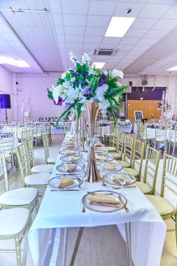 Bir düğün salonundaki çiçek buketleriyle süslenmiş masalardan oluşan bir çatal.