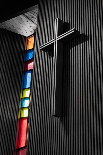 现代教堂的墙上挂着一副彩色玻璃杯的黑色大十字架的垂直截图 — 图库照片