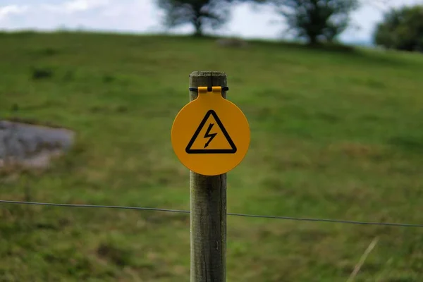 牧草地のフェンスに黄色の高電圧記号のクローズアップショット — ストック写真