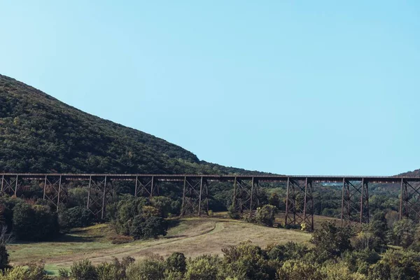 Duży Most Kolejowy Otoczony Zielonymi Drzewami Wzgórzami Błękitnym Niebem Tle — Zdjęcie stockowe