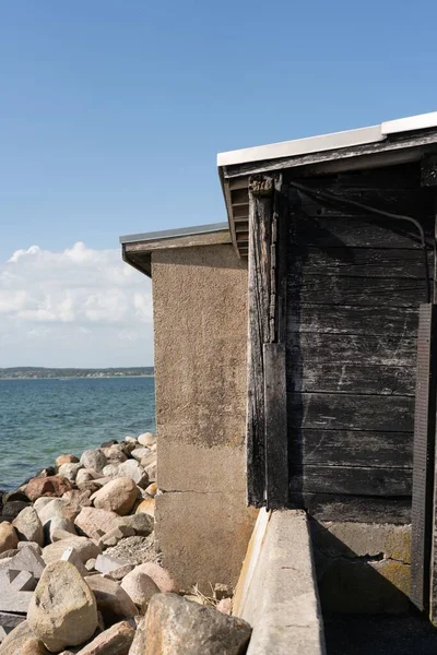 stock image A vertical view of a wooden boat house on a rocky coast, with turquoise water in the background, on a sunny day