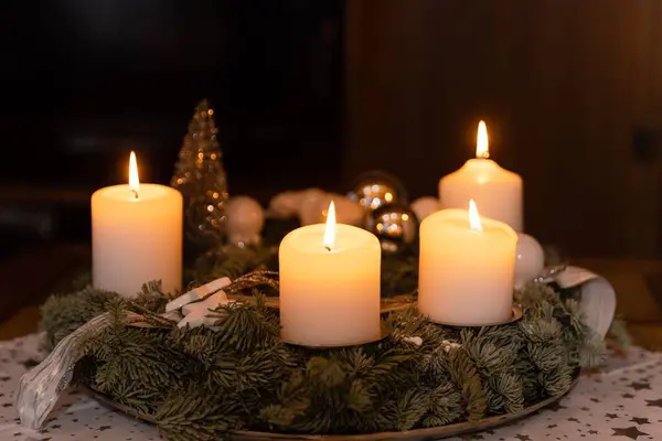 木製のテーブルの上に4本のロウソクが灯され 背景にクリスマスツリーが描かれています — ストック写真