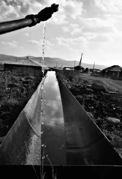 ホースから流れ出た水を灰スケールで撮影した村の金属管に垂直方向 — ストック写真