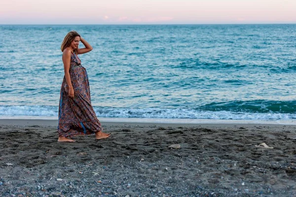 一个穿着裙子在海滨散步的年轻快乐的孕妇 — 图库照片
