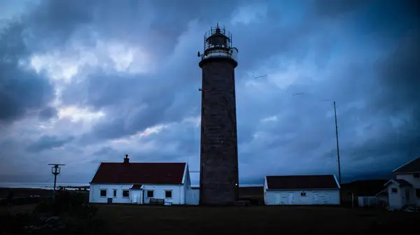 一座巨大的灯塔和白色的建筑物隔离在黑暗的天空下的海岸上 — 图库照片