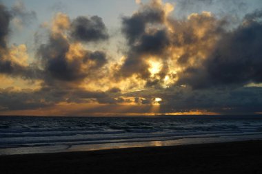 Sahilde güzel bir gün batımı. Arka planda bulutlu bir gökyüzü.