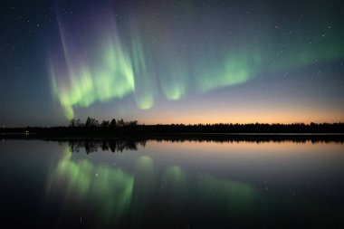 Kutup ışıkları yıldızlı gökyüzünde Laponya, Finlandiya 'daki ormandaki gölün üzerinde.
