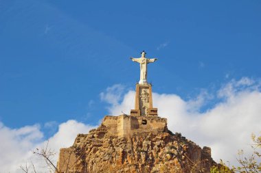 İsa heykeli ve İspanya 'daki Castillo de Monteagudo şatosu mavi gökyüzüne karşı.