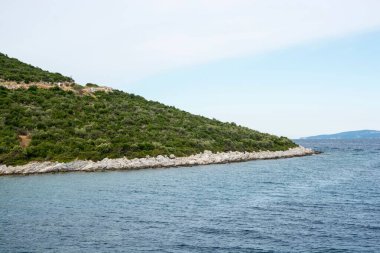 Bulutlu bir gökyüzüne karşı kayalık dağlarla çevrili büyüleyici bir göl manzarası.