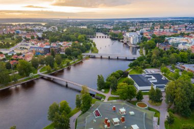 Gün batımında bulutlu gökyüzü arka planında nehir ve eski binalar olan bir kasabanın hava görüntüsü.