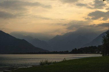 Gün batımı manzarası. Como Gölü üzerinde çimenli ve siluetli dağlar, İtalya.