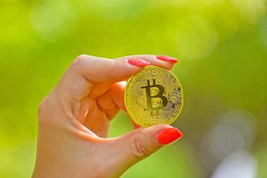 Bulanık bir arkaplanda altın bir Bitcoin tutan bir kadının yakın çekimi.