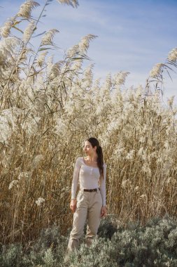 Gölün kıyısında yetişen uzun kamışların yanında poz veren genç ve şık bir kadının dikey çekimi.