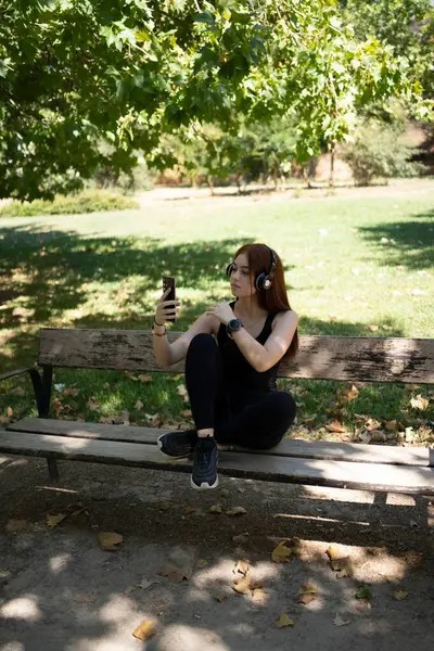 公園の晴れた夏の日にヘッドフォンでスマートフォンや音楽を聴いている女の子 — ストック写真