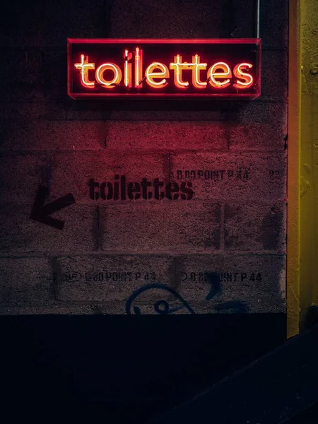 フランスのナントの落書きのテキストに沿って壁にかかってネオンのトイレの看板の垂直ショット — ストック写真