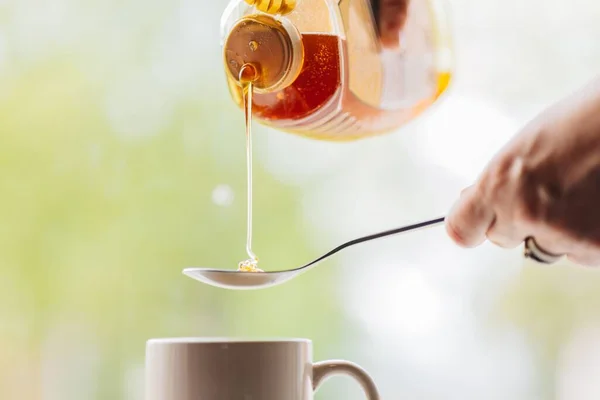 stock image A closeup shot of a person pouring natural honey into a spoon to put into morning tea