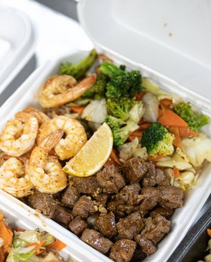 Masanın üstünde biftek, salata ve karides olan bir beslenme çantasının dikey görüntüsü.