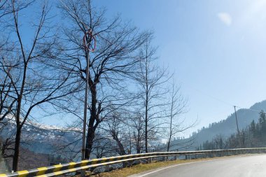 Dağlarda kar ve ağaçlar mavi gökyüzü ve bulutlar bir arka plan üzerinde yolun kenarında kaplı asfalt yoldan doğal kış görünümü