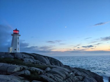 Gün batımında arka planda deniz olan kayalık sahilde bir deniz feneri.