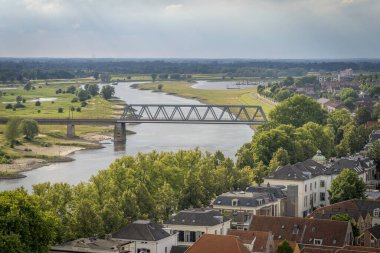 Hollanda Deventer şehrinde nehir üzerinde gri ve kahverengi çatılı evler manzaralı bir köprü.